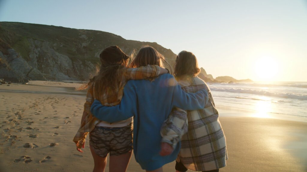 three best friends walk on sunny beach at sunset happy laughing women hug and put arms sbi 351349617